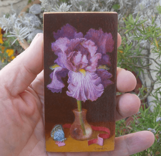 Small format oil painting of a still life with an iris in a translucent glass vial